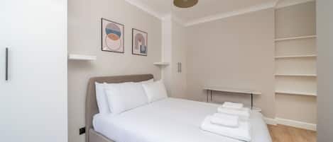 Un dormitorio ordenado con una cama grande, una mesita de noche, una lámpara colgante y dos obras de arte en la pared.