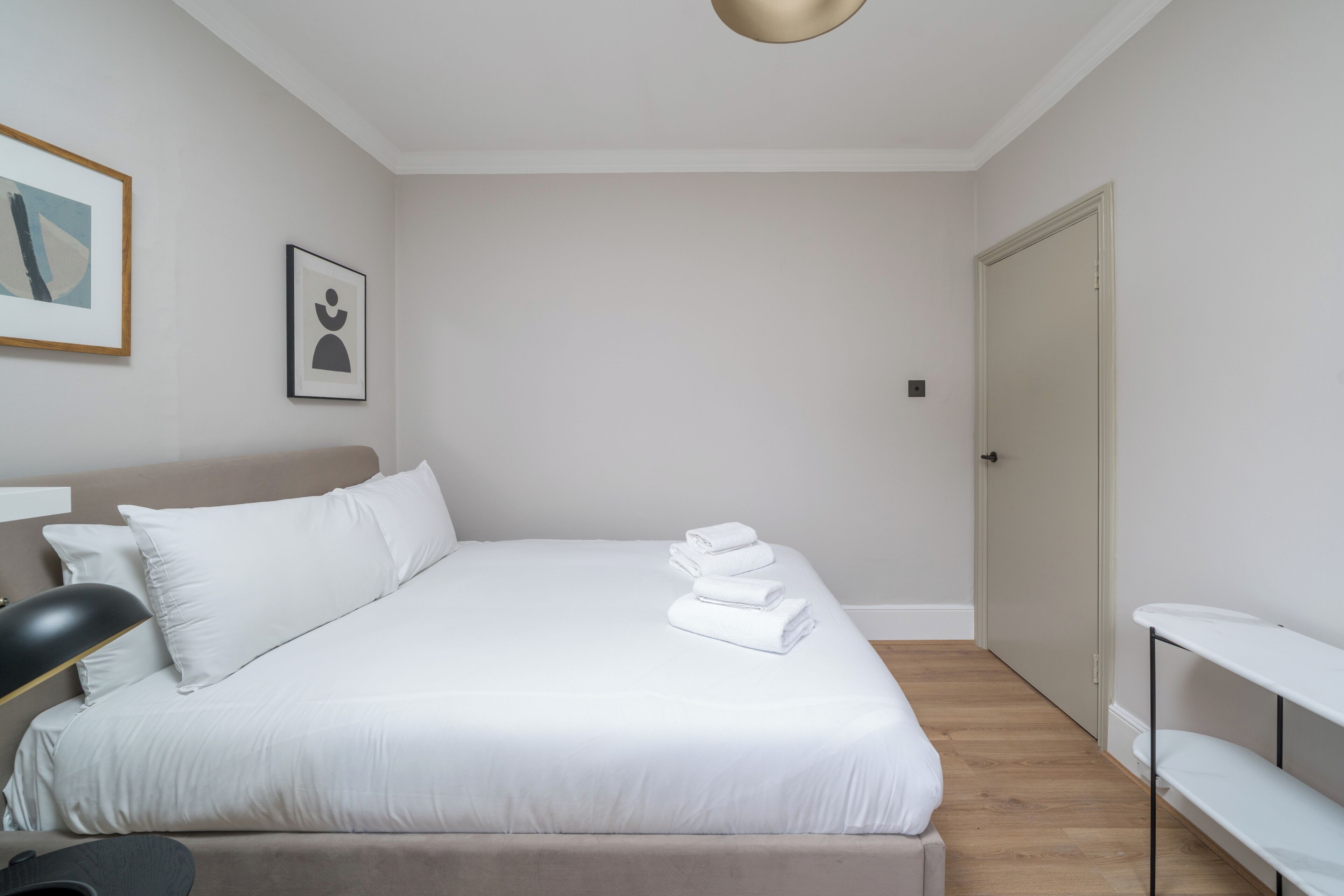 A neatly made bed with white linens and towels, a bedside lamp, and a framed picture on the wall.