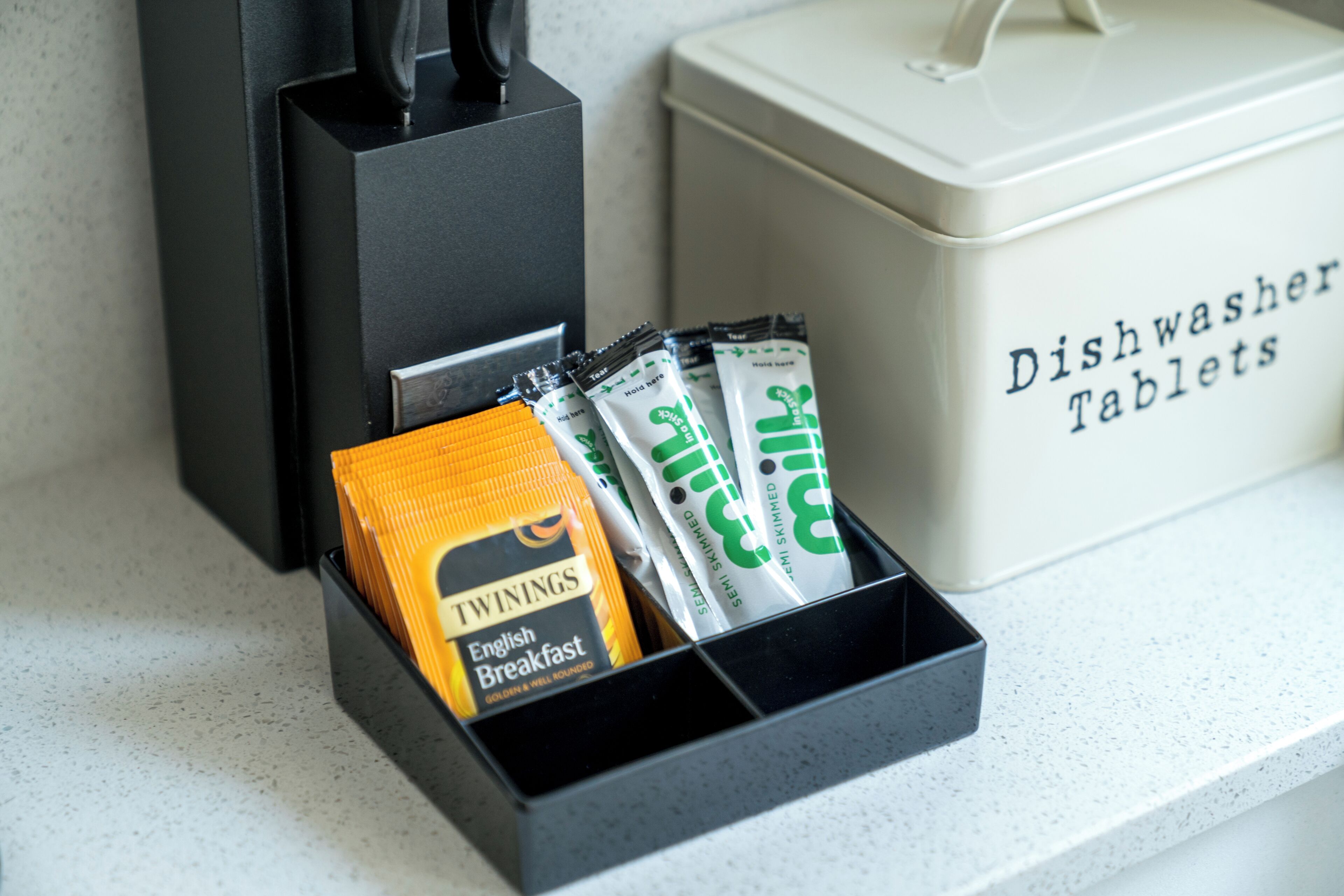 Ein schwarzes Tablett mit Twinings English Breakfast Tee und Twinings Tee-Tabletten, neben einem Behälter für Geschirrspültabletten.