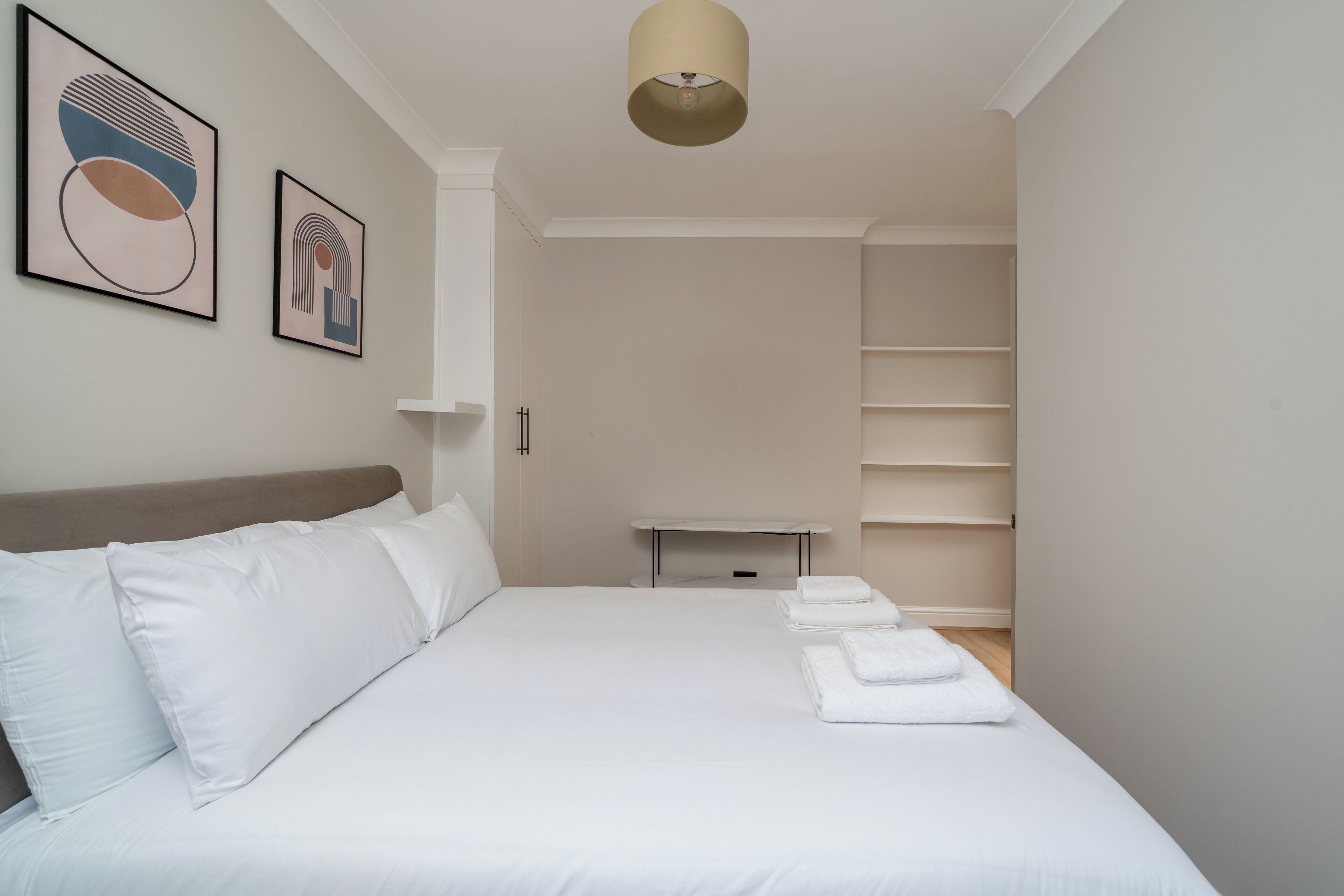 A neatly arranged bedroom with a bed, pillows, a bedside table, and a shelf unit.