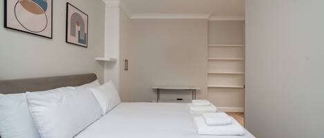 A neatly arranged bedroom with a bed, pillows, a bedside table, and a shelf unit.