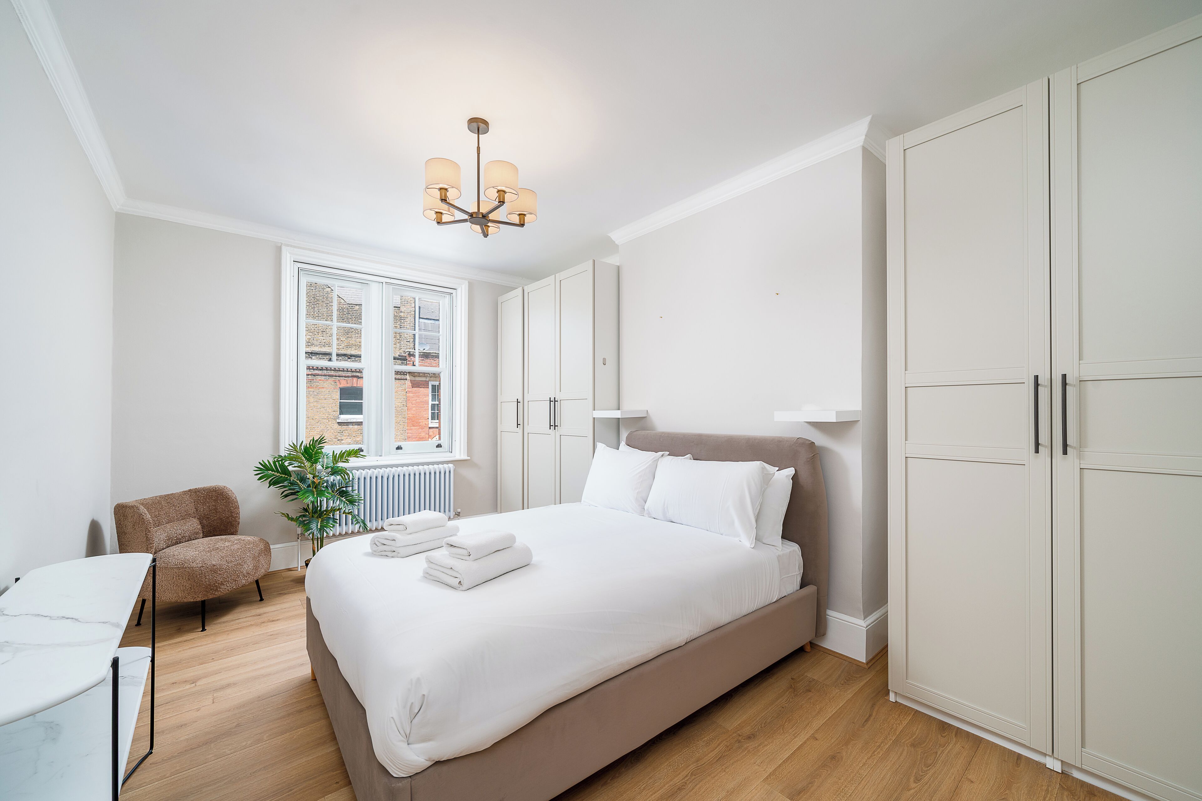 A bedroom with a bed, a chair, a desk, and a large wardrobe.