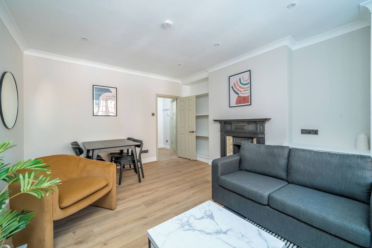 A living room with a sofa, a coffee table, a dining table with chairs, and a fireplace.