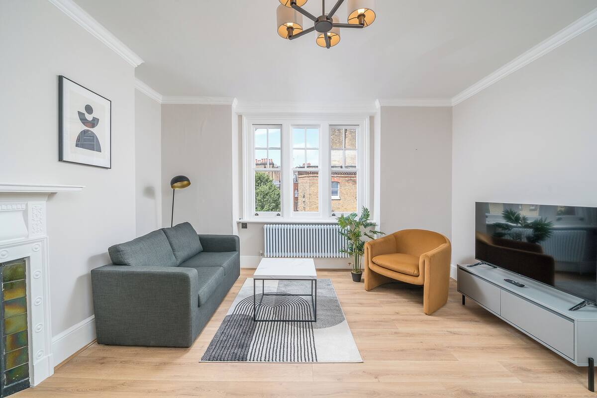 A modern living room with a grey sofa, a small white coffee table, a yellow armchair, and a TV on a grey cabinet.