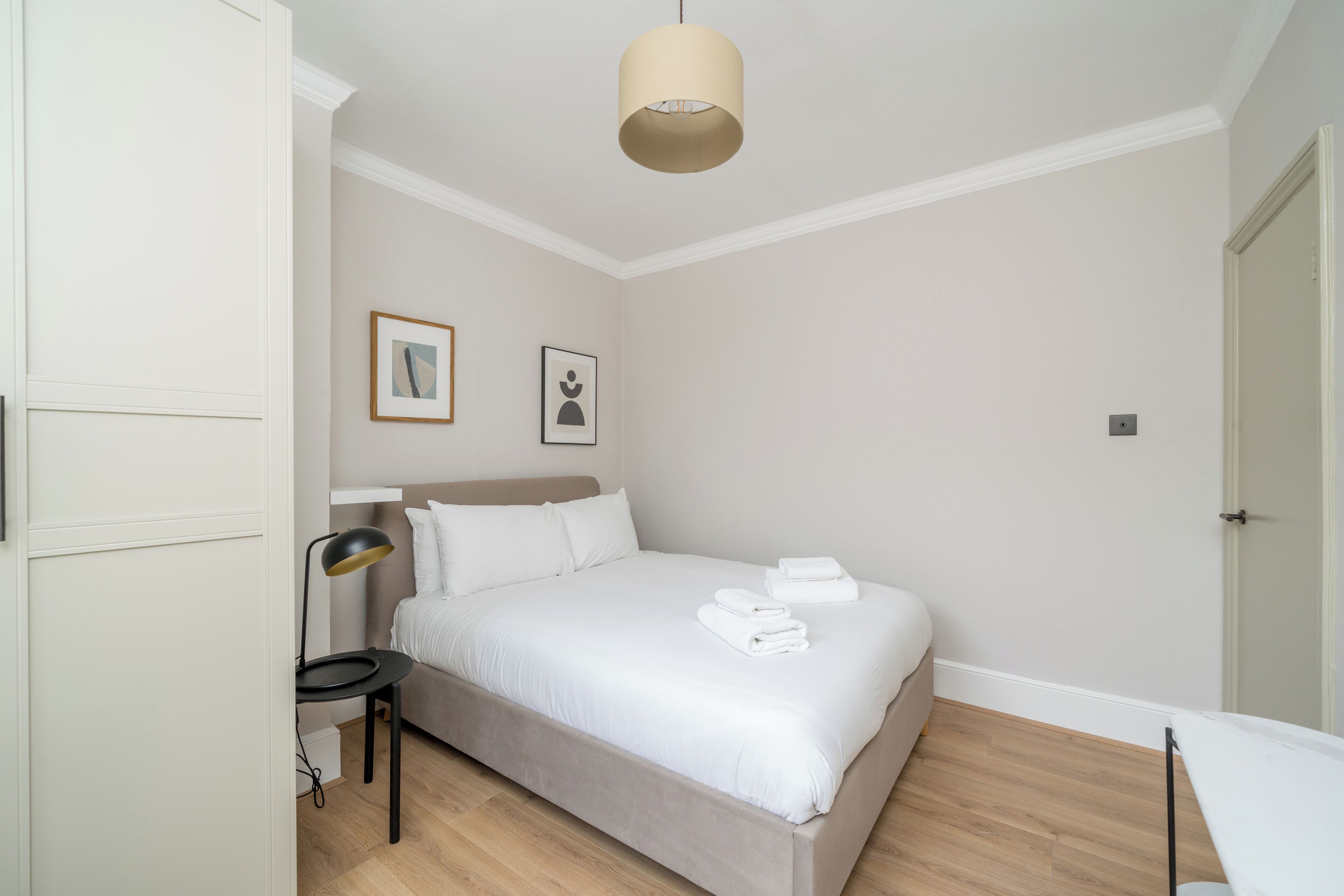 A neatly arranged bedroom with a bed, bedside lamp, and two framed pictures on the wall.