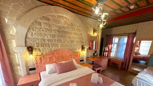 Ein Schlafzimmer mit Steinsandsteinwand, Holzbalkendecke, einem Bett mit rosa Bettwäsche, einem Nachttisch, einem Spiegel und einer Bank.