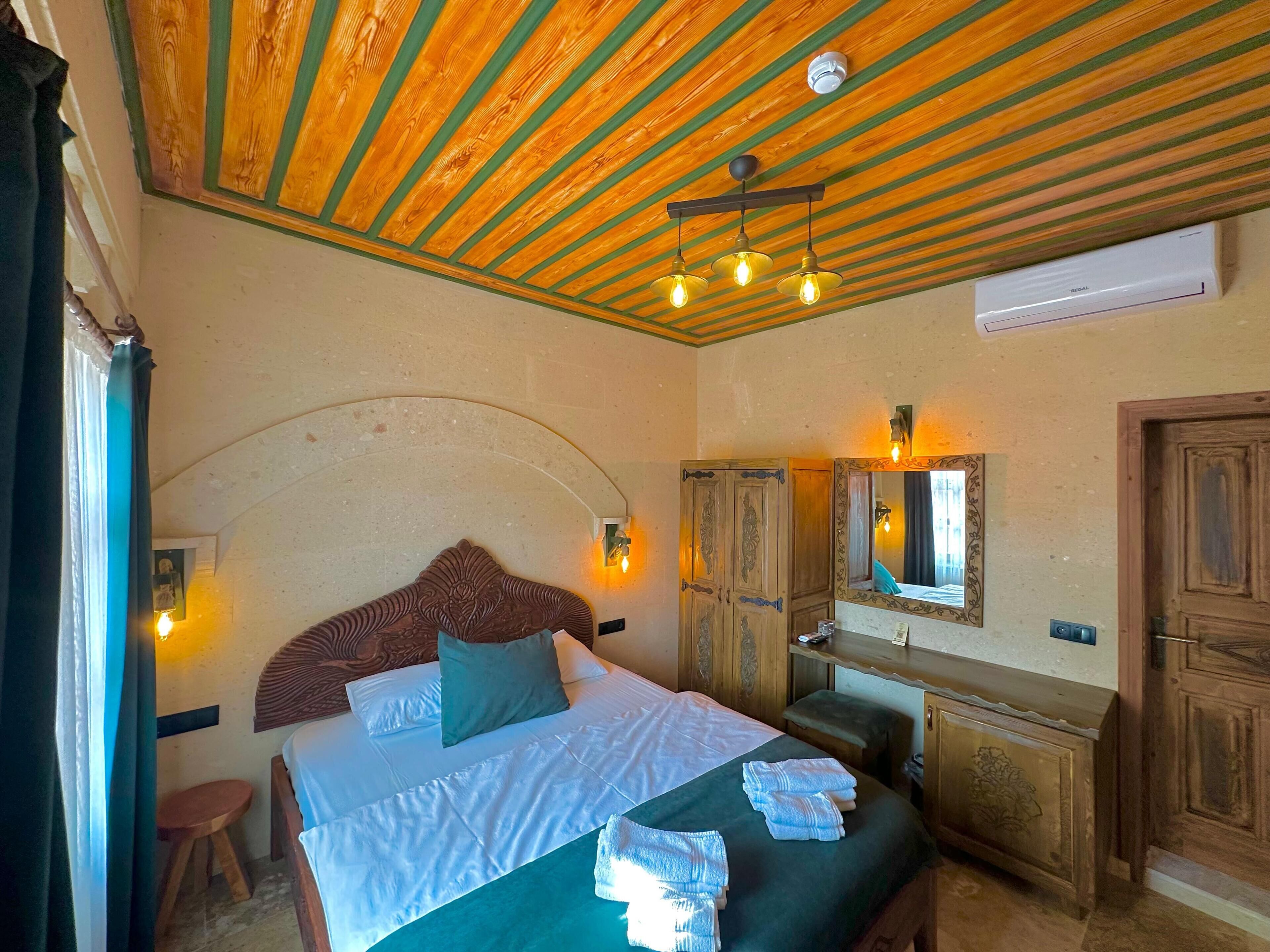 Camera da letto con soffitto in legno, un letto con cuscini, un comodino, uno specchio e un condizionatore d'aria a parete.