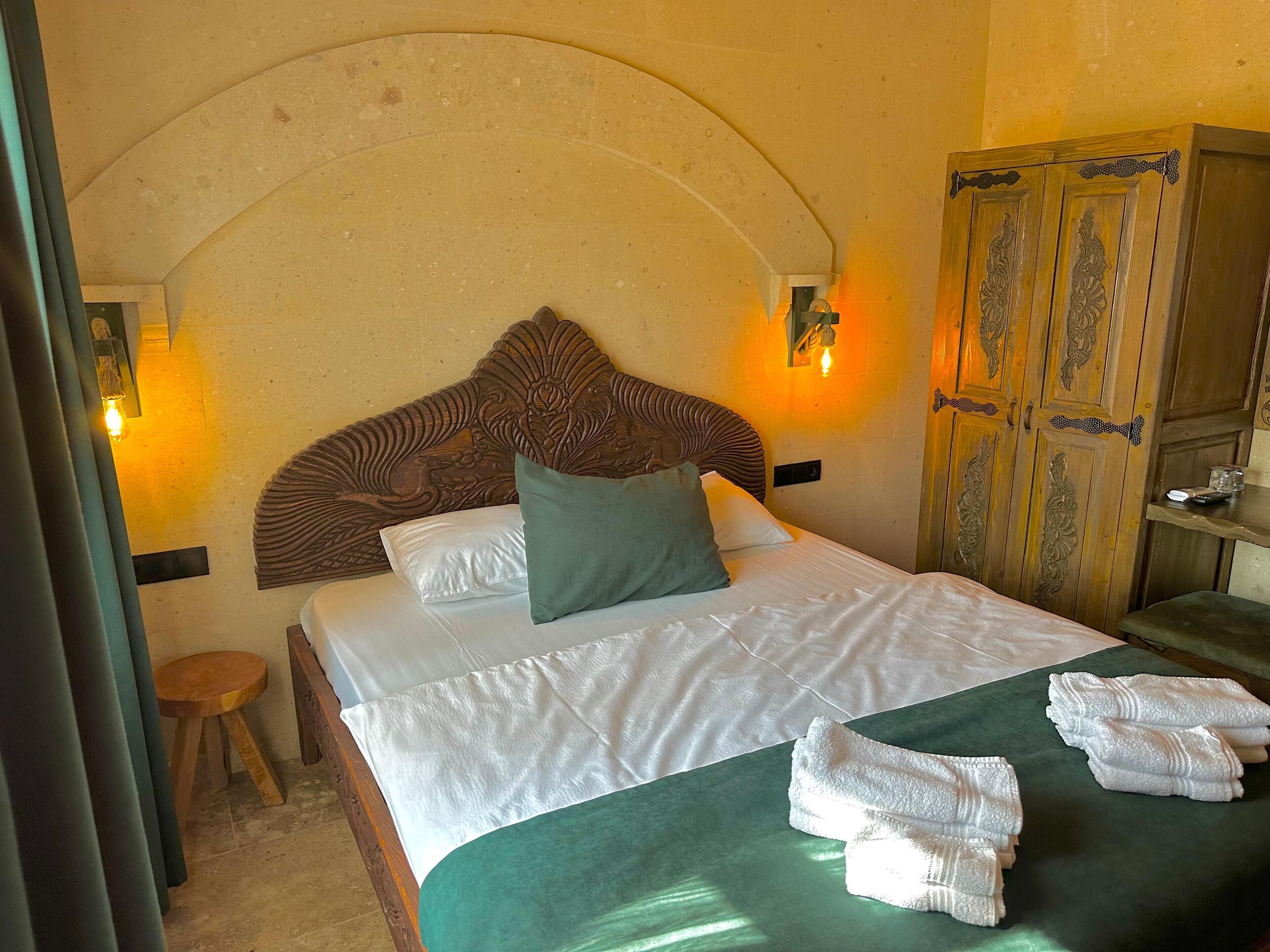 A hotel room with a bed, pillows, a green bedspread, and towels.