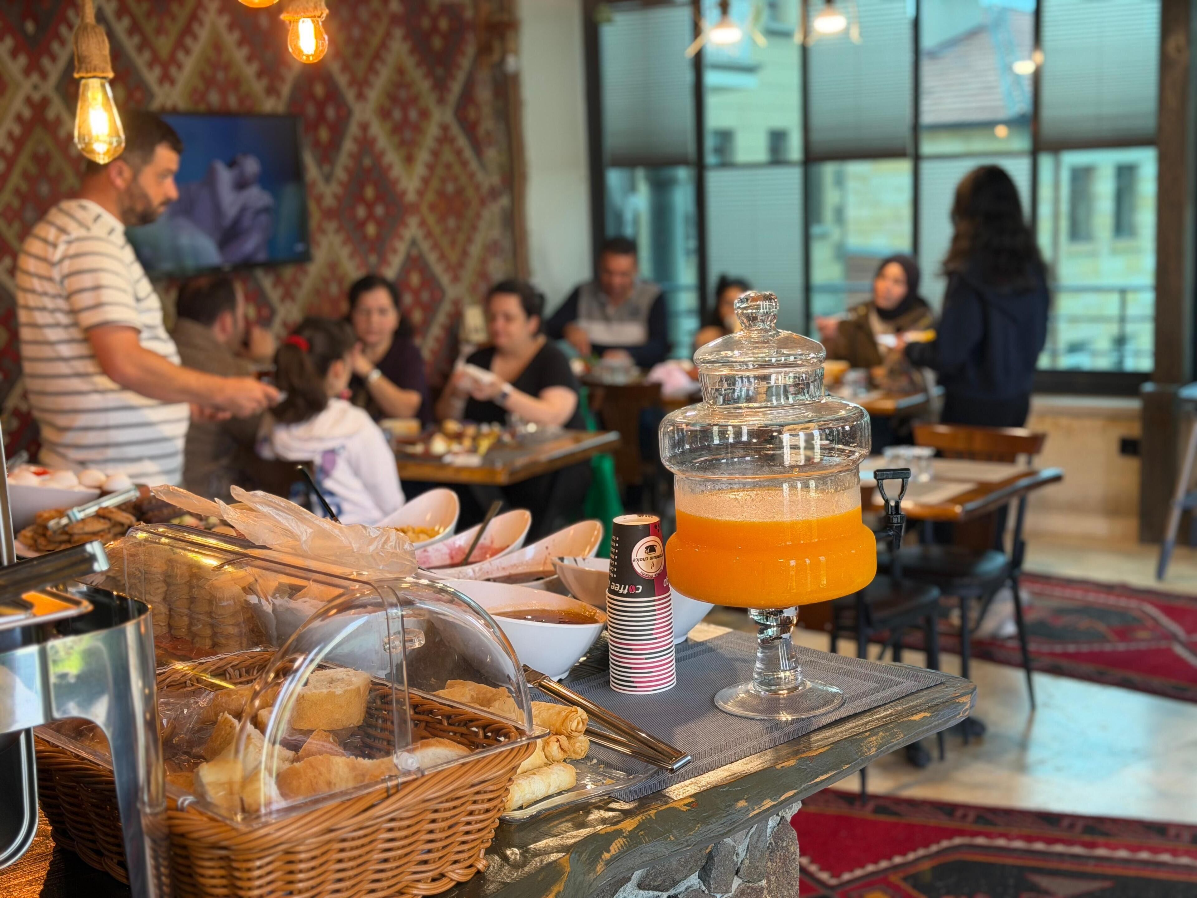 Un bufé de desayuno con pan, bollería y dispensador de bebidas.