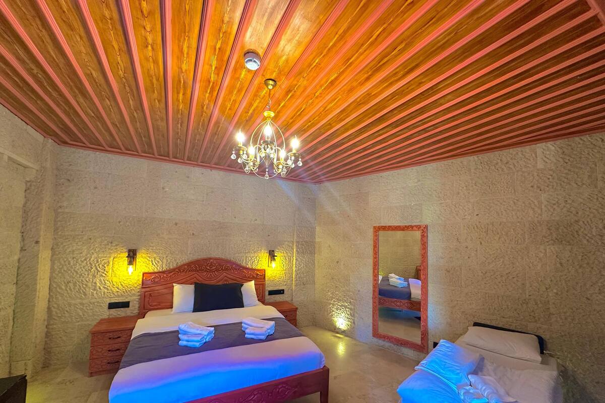 Ein Schlafzimmer mit Holzbalkendecke, einer Chandelier, einem Bett mit Kopfteil, Nachttischen, einem Spiegel und einem kleinen Beistelltisch mit Handtüchern.