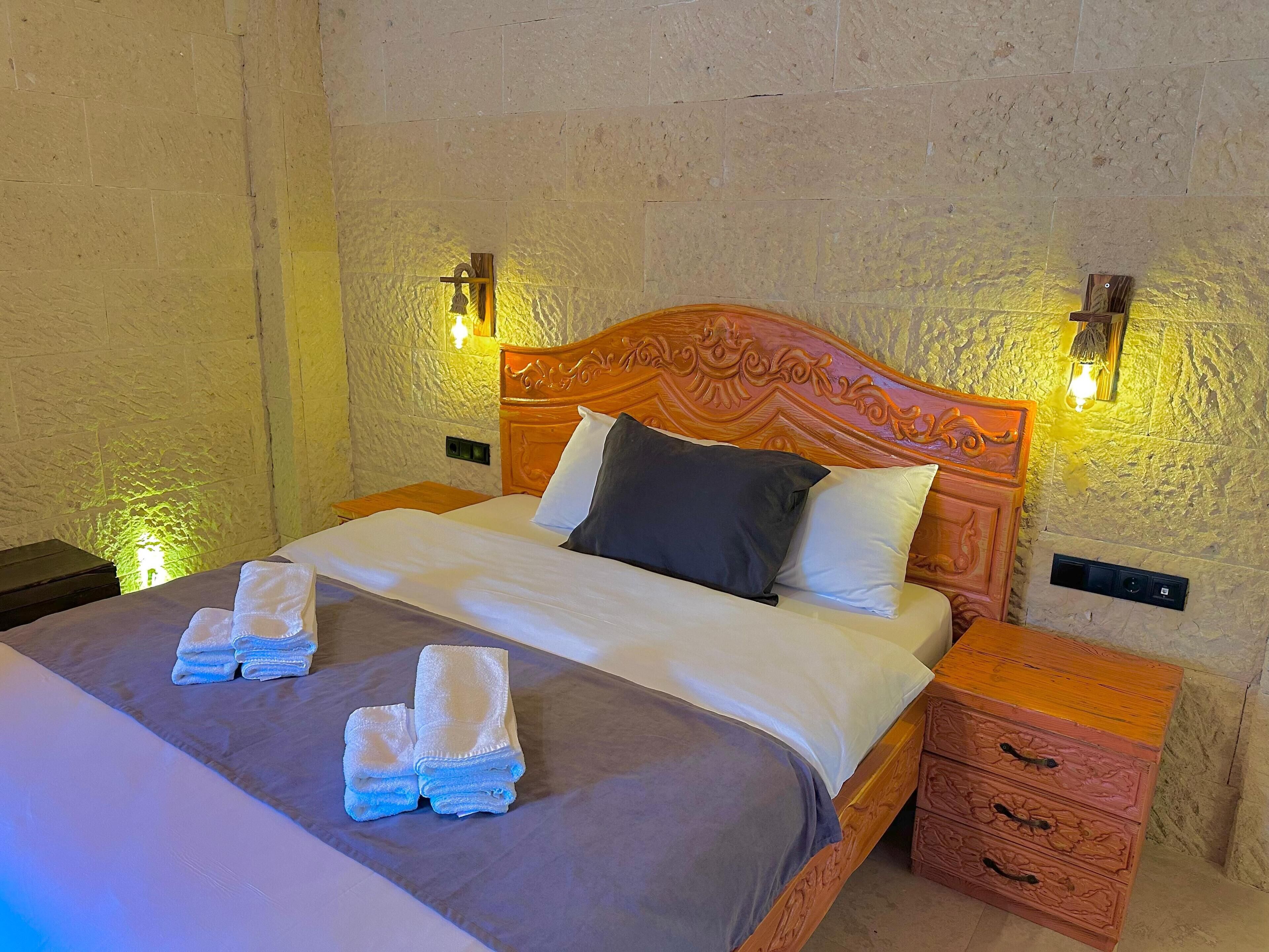 A neatly made bed with a wooden headboard, two bedside tables, and a wall-mounted light fixture.