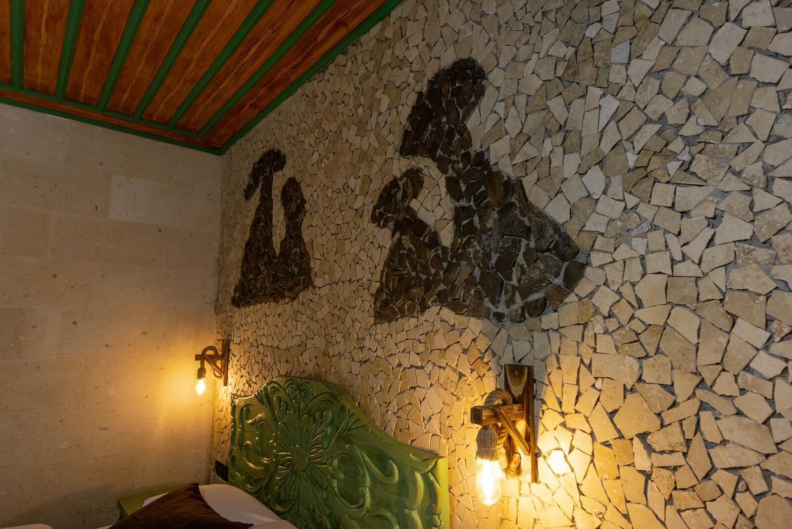 Une pièce avec un mur décoré de mosaïques, une tête de lit verte et deux lampes fixées au mur.