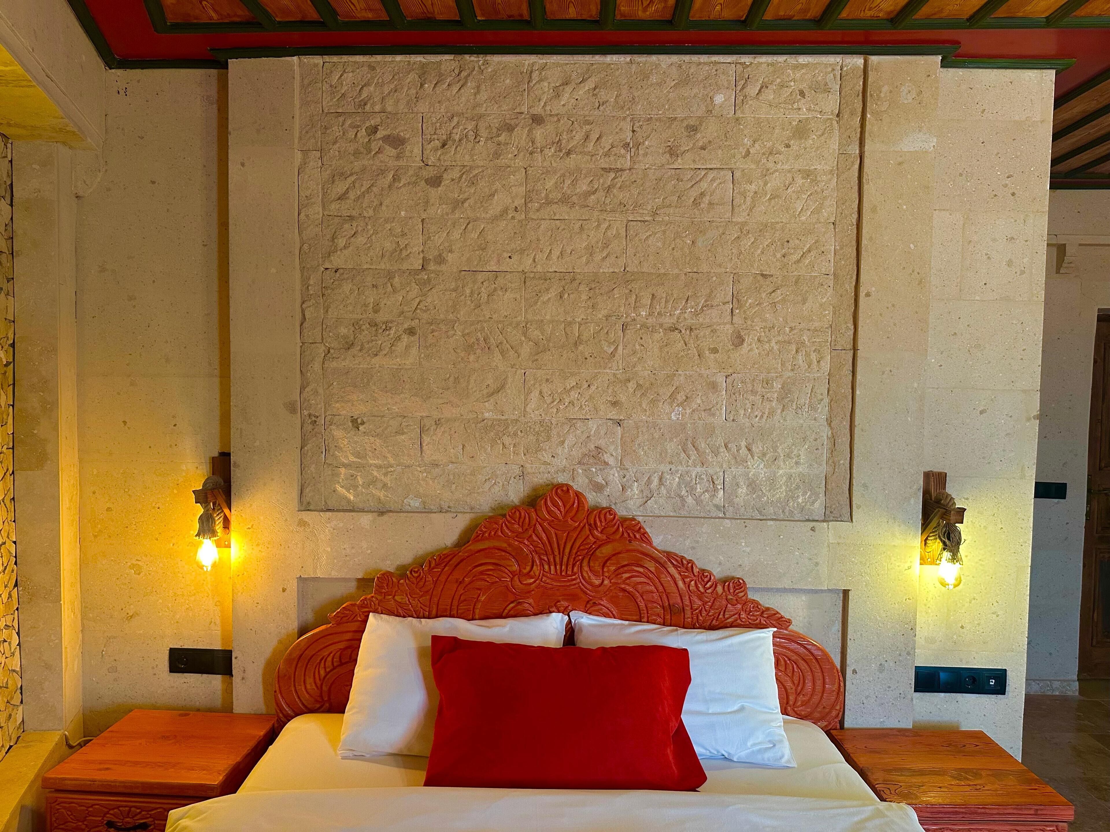 Habitación de hotel con pared de piedra, cabecero de madera y dos lámparas fijadas a la pared.