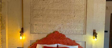 Habitación de hotel con pared de piedra, cabecero de madera y dos lámparas fijadas a la pared.