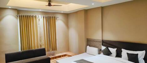 A modern hotel room with a large bed, a sofa, a ceiling fan, and a window with curtains.