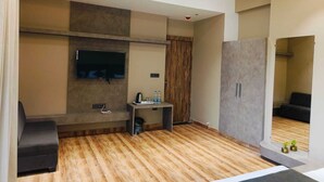 A modern living room with a flat-screen TV mounted on the wall, a sofa, a coffee table, and a cabinet. - Hotel Maple Residence (Udaipur)