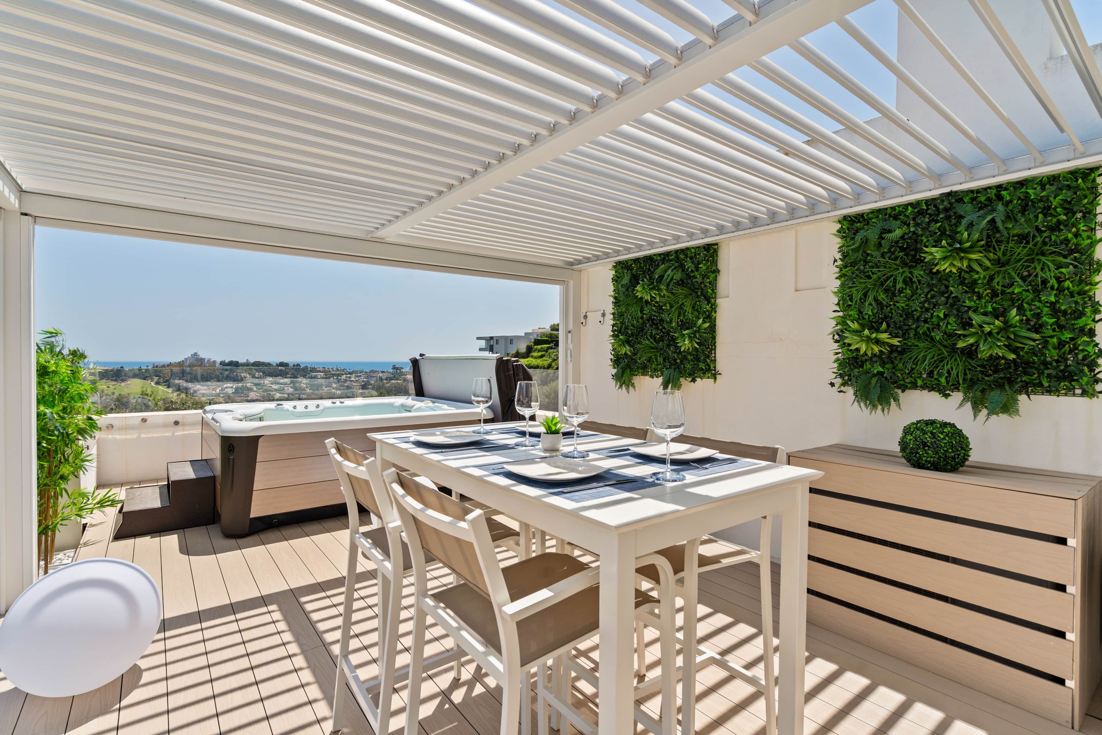 A covered outdoor area with a table set for dining, a hot tub, and a view of the sea.