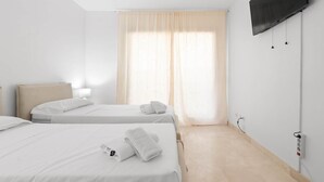 A hotel room with two beds, a TV mounted on the wall, and a window with curtains.