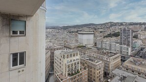 A high-rise building with multiple floors, large windows, and a view of a cityscape with various buildings and a distant hill.