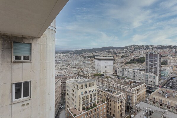 A high-rise building with multiple floors, large windows, and a view of a cityscape with various buildings and a distant hill.