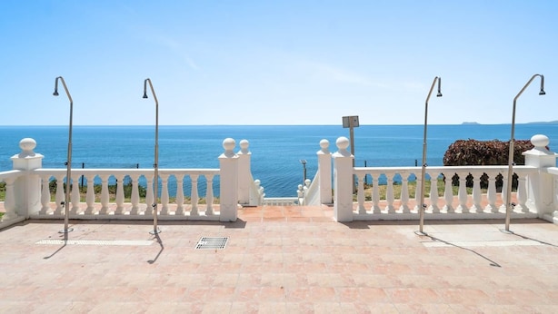 A balcony with a view of the sea, white balustrades, and a tiled floor.