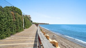 A wooden boardwalk along a beach with a fence on one side and buildings in the background.