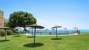 A pool area with umbrellas, a lifebuoy, and a view of the sea.