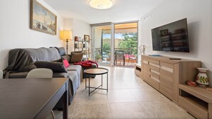 A modern living room with a sofa, coffee table, TV, and a balcony with outdoor furniture.