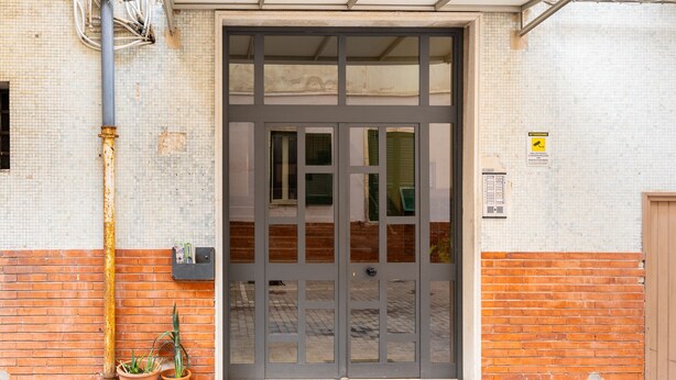 A large metal door with glass panels, flanked by brick walls and potted plants. - Bacchilide Novanta by Wonderful Italy (Siracusa)