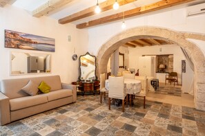 A living room with a sofa, a dining table with chairs, a mirror, and a stone archway leading to another room.