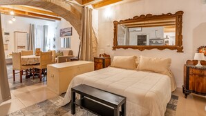 Camera da letto con un letto grande, una testiera in legno, uno specchio e un arco in pietra che conduce al bagno.