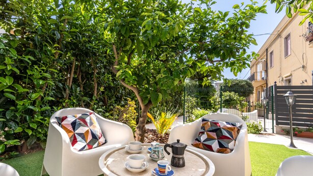 Un área de estar al aire libre con una mesa redonda, dos sillas blancas y una cafetera.