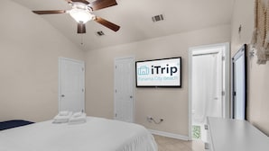 A hotel room with a bed, a ceiling fan, a TV screen displaying 'iTrip Panama City Beach', and a door leading to another room. - Pier Atlas (Panama City Beach)