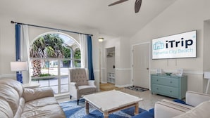 A hotel room with a large window, a ceiling fan, a bed, a sofa, a coffee table, and a desk with a lamp. - Pier Atlas (Panama City Beach)