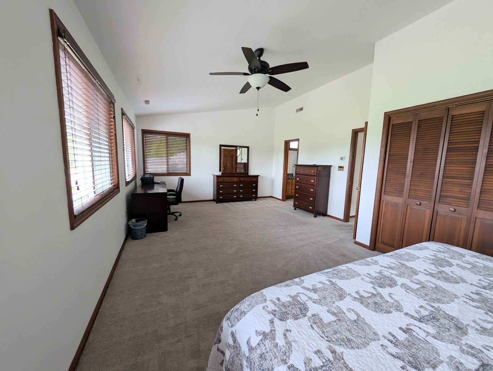 Ein Schlafzimmer mit Bett, Schreibtisch, Kommode, Deckenventilator und Kleiderschrank.