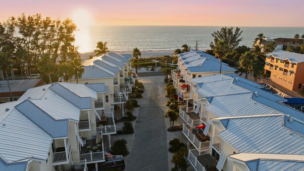 A beachfront hotel with multiple-story buildings, a central courtyard, and a view of the ocean.