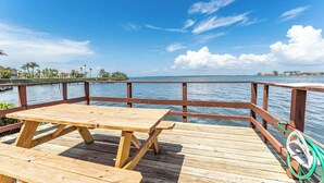 A wooden deck with picnic tables overlooking a body of water, a railing, and a hose.