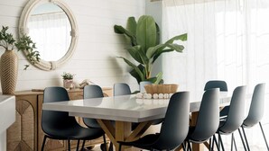 A dining area with a round table, black chairs, a white tablecloth, a woven basket with white spherical objects, and a large green plant.