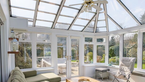 A conservatory with a glass ceiling, a wooden table, a cushioned sofa, and a chair.