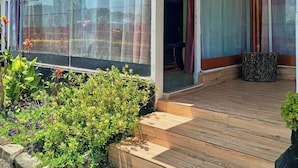 Katettu ulkoalue, jossa on puinen terassi, lasiseinäinen tila ja kyltti, joka ilmoittaa, että alueella on vuokrattavana mökki.