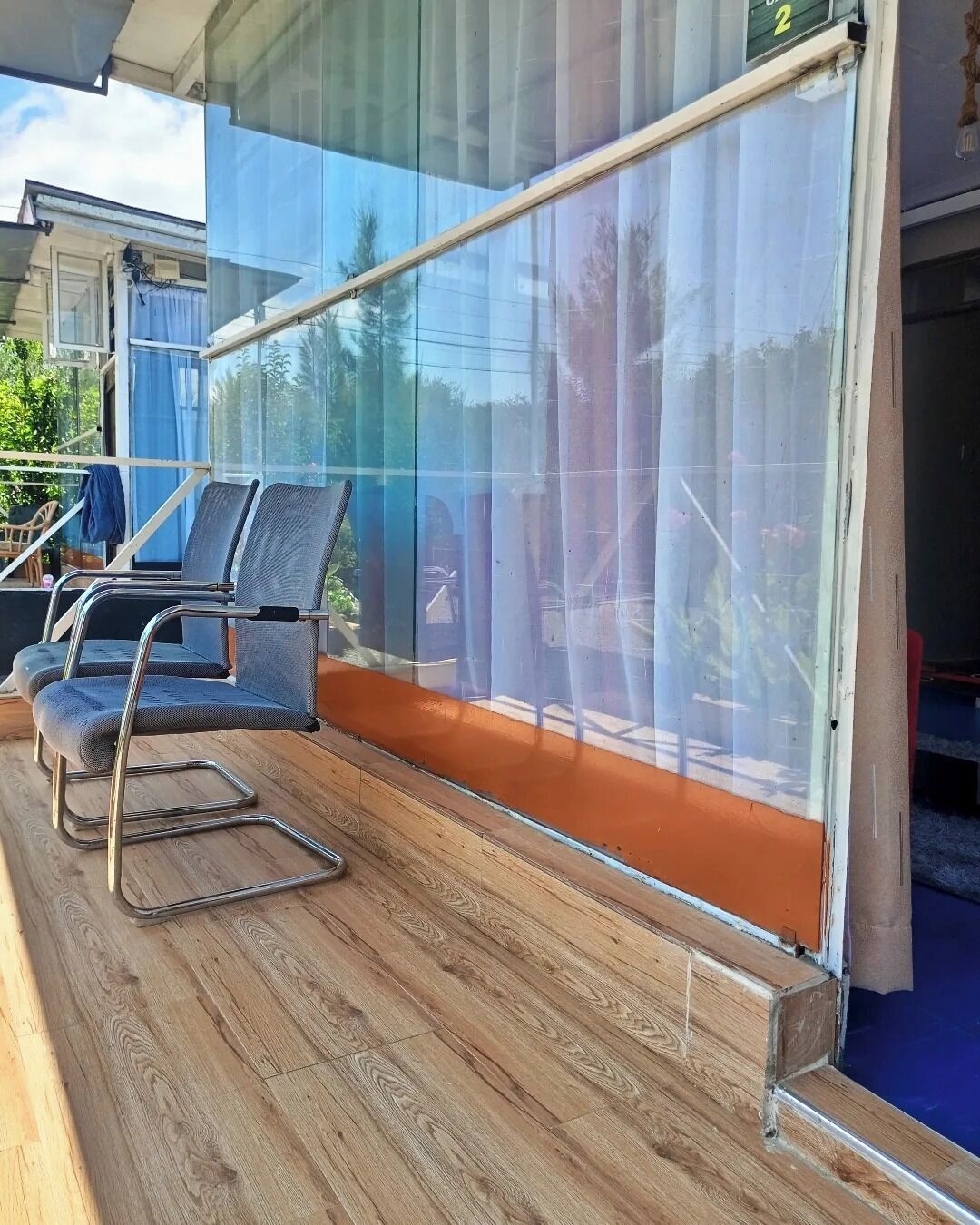 A balcony with a glass barrier, wooden flooring, and two upholstered chairs.