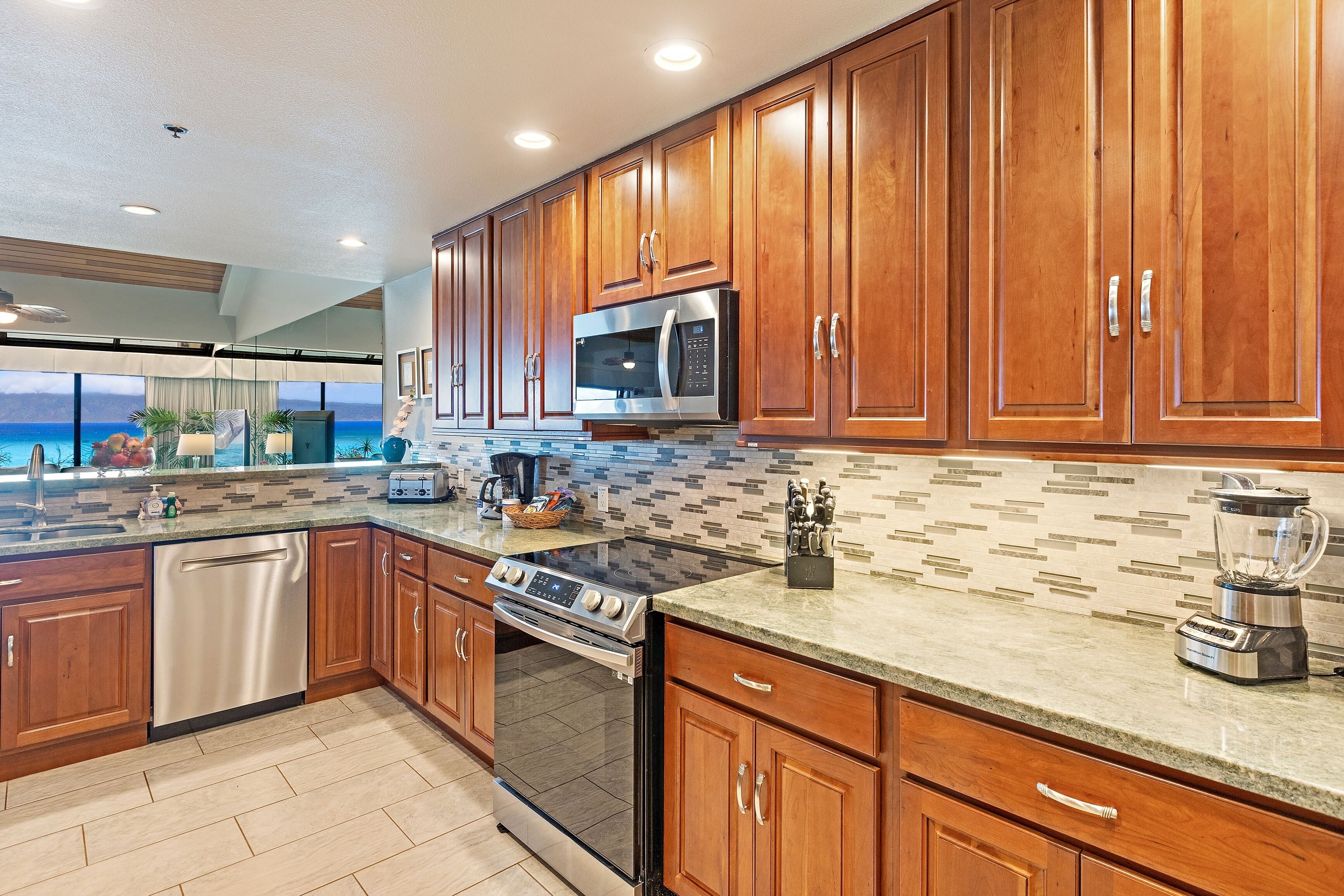 A modern kitchen with wooden cabinets, stainless steel appliances, and a view of the ocean.