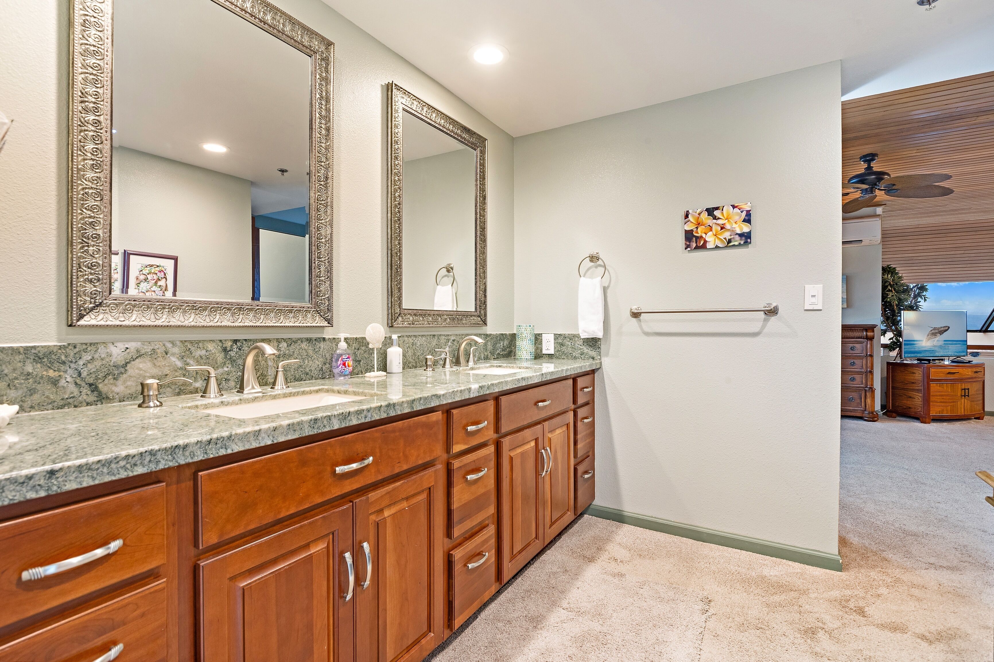A bathroom with two large mirrors, a granite countertop, wooden cabinets, and a towel rack.