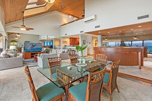 Amplia sala de estar con mesa de comedor de vidrio, asientos cómodos, un televisor grande y vista al océano.