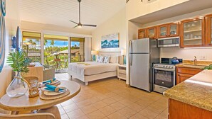 A modern kitchen with a refrigerator, microwave, and stove. There is a dining area with a table and chairs, and a bed with a view of the outdoors. - Napili Shores G258 Studio Condo Condo (lahaina)