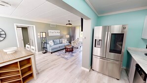 A modern kitchen with a stainless steel refrigerator, a wooden dining table with a bowl, and a blue sofa in the living area.