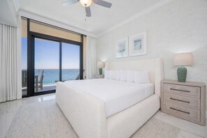 A hotel room with a large bed, a ceiling fan, a nightstand with a lamp, and a view of the ocean through a sliding door. - Phoenix Gulf Shores Ii 1805 2 Bedroom Condo (Gulf Shores)