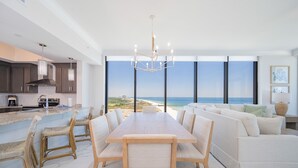 Eine moderne Küche mit einer großen Kochinsel, ein Essbereich mit Blick auf den Strand und ein Wohnbereich mit Sofa und Lampe.