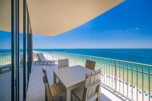 Een balkon met een tafel en stoelen, met uitzicht op een strand en helderblauw water.