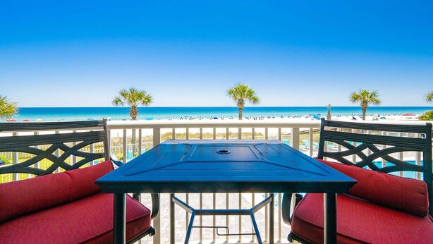 A balcony with a table and chairs overlooking a beach. - Tradewinds 102 1 Bedroom Condo (Orange Beach)
